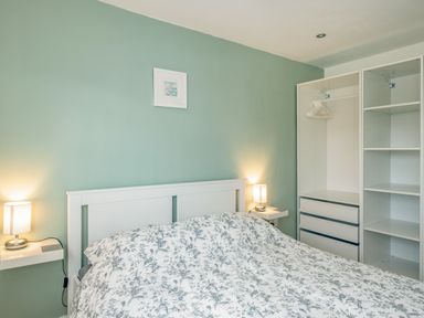 A bedroom with a bed a floral duvet two bedside lamps and an open wardrobe at Shrimper's Cottage in Tredrizzick near St Minver