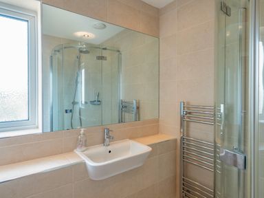 A bathroom with a sink and mirror next to a glass shower enclosure and heated towel rail at Shrimper's Cottage in Tredrizzick near St Minver