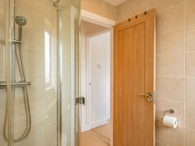 A bathroom with a glass shower enclosure wooden door and toilet paper holder at Shrimper's Cottage Tredrizzick near St Minver