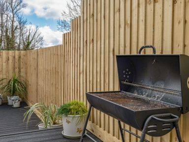 A barbecue grill and several potted plants on a wooden deck with a tall wooden fence in the background at Shrimper's Cottage Tredrizzick near St Minver