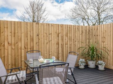 A patio area with a glass table and four chairs with cushions and potted plants at Shrimper's Cottage in Tredrizzick near St Minver