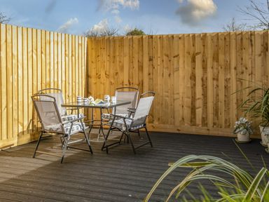 An outdoor patio area with a glass table and four chairs surrounded by wooden fencing at Shrimper's Cottage in Tredrizzick near St Minver