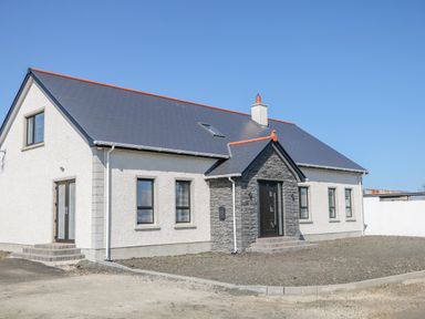 A single story house with a dark roof and stone entrance in a gravel yard at SJs Cottage in Castlerock