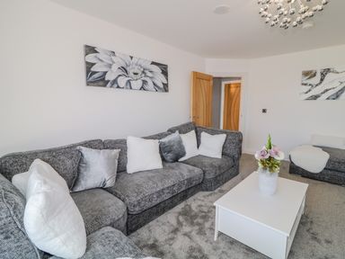 A living room with a grey sofa white cushions a white coffee table with a vase of flowers and wall art at SJs Cottage in Castlerock