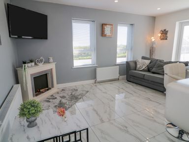 A living room with a mounted TV fireplace sofa and two windows at SJs Cottage Castlerock