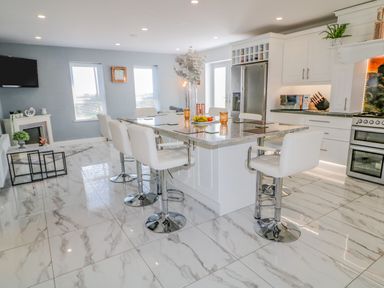 A kitchen with a large island and white chairs on marble floor at SJs Cottage in Castlerock