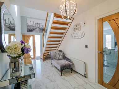An entryway with a glass table holding flowers a wooden staircase a chaise lounge under the stairs and wooden doors at SJs Cottage in Castlerock