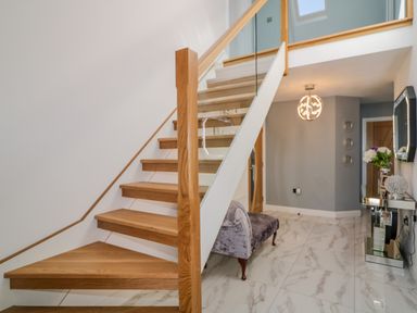 A staircase with wooden steps and glass railing in a hallway with marble tiled floor and a mirrored console table at SJs Cottage in Castlerock
