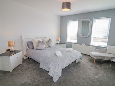 A bedroom with a bed two side tables with lamps a sofa a hanging ceiling light and two windows at SJs Cottage in Castlerock