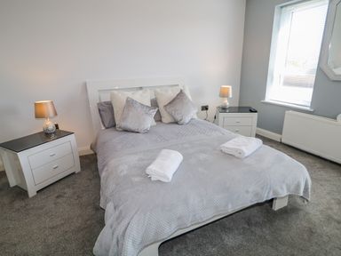 A bedroom with a double bed and pillows two bedside tables with lamps a window with blinds and a radiator at SJs Cottage in Castlerock