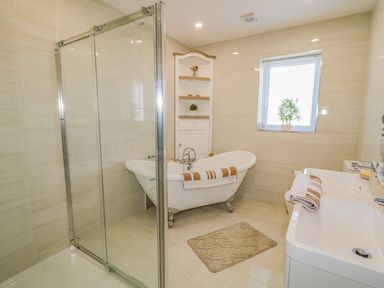 A bathroom with a clawfoot bathtub shower enclosure sink and a window with a plant at SJs Cottage in Castlerock