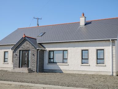 A single story house with stone entrance and multiple windows at SJs Cottage in Castlerock