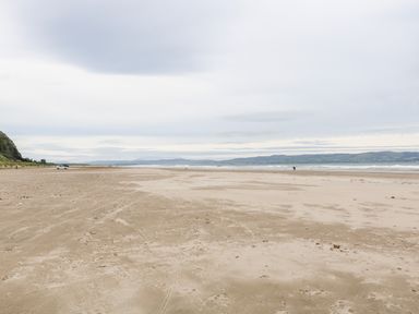 A sandy beach with a few people and a car near cliffs and hills at SJs Cottage in Castlerock