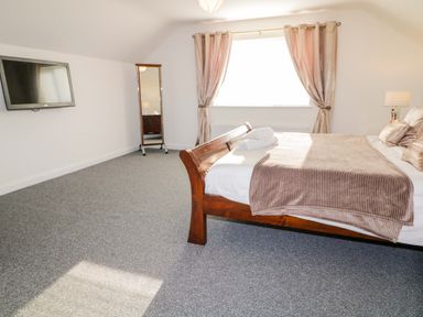 A bedroom with a wooden bed with bedding a wall-mounted television a standing mirror and a window with curtains at SJs Cottage in Castlerock