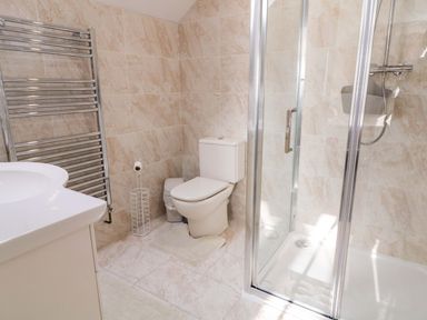A bathroom with a toilet, shower enclosure, sink, towel rack, and tiled walls at SJs Cottage in Castlerock