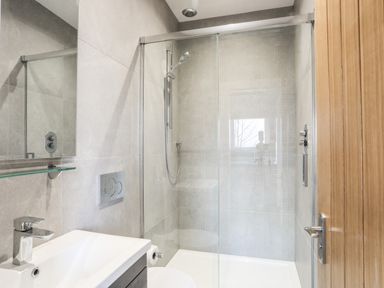 A bathroom with a walk-in shower a sink with a faucet and a wooden door at Hilltop Lodge in Corwen