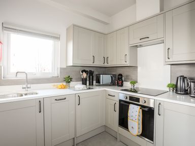 A kitchen with grey cabinets a window a sink a stove microwave kettle and small plants at Hilltop Lodge in Corwen