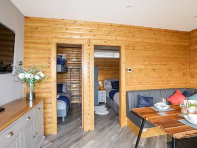 A dining area with a wooden table and bench seating next to two doorways leading to bedrooms at Hilltop Lodge in Corwen