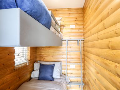 A bedroom with wooden walls, a bunk bed with a blue pillow and a window with blinds at Hilltop Lodge in Corwen