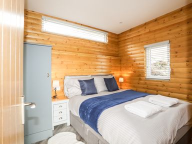 A bedroom with a double bed with blue and white bedding two bedside lamps a blue wardrobe and wooden walls at Hilltop Lodge in Corwen