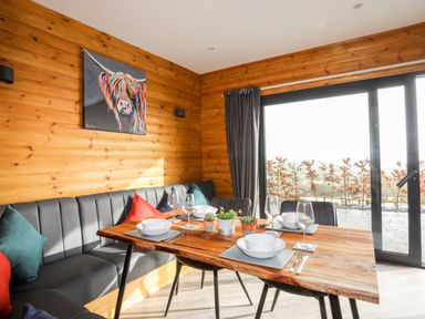 A dining area with a wooden table set with bowls wine glasses and cutlery beside a bench and chairs with cushions at Hilltop Lodge in Corwen