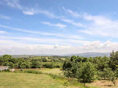 A grassy field with trees and hills under a partly cloudy sky at Hilltop Lodge in Corwen
