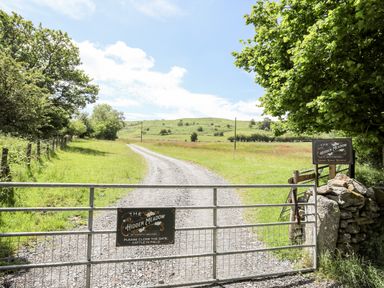 A metal gate at the entrance to a gravel path leading through a meadow with trees and hills in the distance at The Hidden Meadow