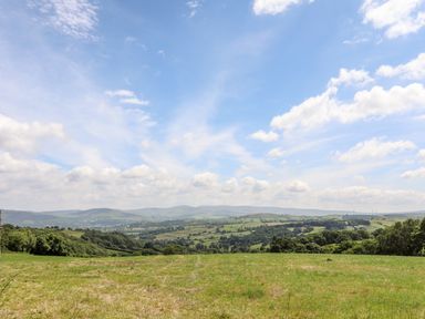 A grassy field with rolling hills and trees under a partly cloudy sky at Hilltop Lodge in Corwen