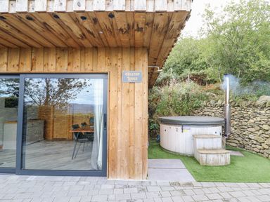 A wooden lodge exterior with sliding glass doors next to a hot tub with steps and a chimney at Hilltop Lodge in Corwen
