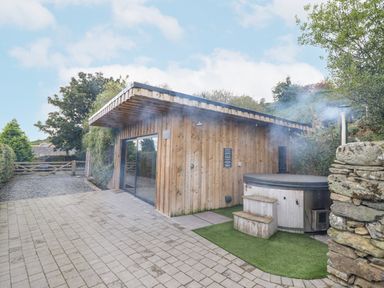 An outdoor area with a wooden building and a hot tub emitting steam at Hilltop Lodge in Corwen