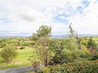 A countryside landscape with green fields trees and hills under a partly cloudy sky at Hilltop Lodge in Corwen