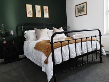 A bedroom with a black metal bed frame white bedding and pillows brown blanket and framed pictures on the walls at No.37 in Beverley