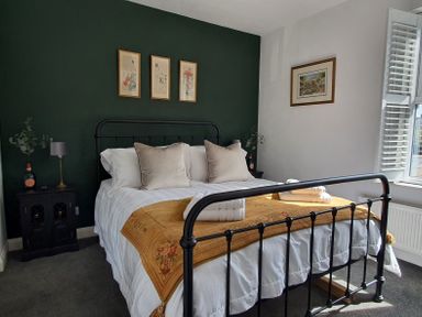 A bedroom with a black metal bed frame white bedding mustard colored throw pillows and framed pictures on the walls at No.37 in Beverley