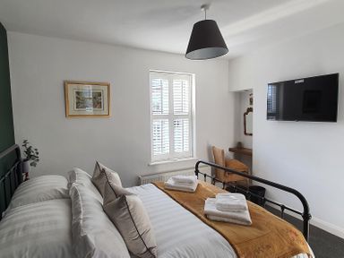 A bedroom with a double bed folded towels on it a television a chair and a window with shutters at No.37 in Beverley