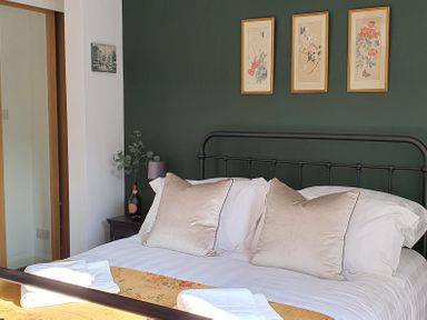 A bedroom with a bed with white bedding and beige pillows against a dark green wall with three framed floral prints at No.37 in Beverley