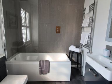 A bathroom with a bathtub with a towel on the side a stool with folded towels and a towel warmer at No37 in Beverley