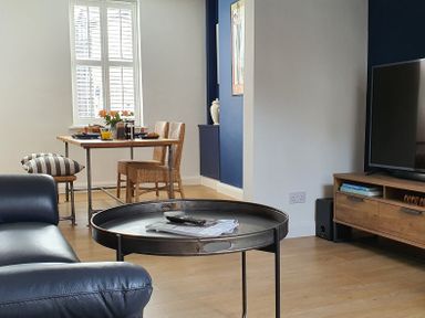 A living room with a round metal coffee table a leather sofa a dining table with chairs and a television on a wooden stand at No.37 in Beverley