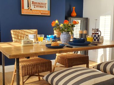 A dining table set with blue plates cups and glasses with orange juice croissants and a flower vase in a room with wicker chairs and a blue wall at No 37 in Beverley