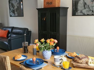 A dining table set with plates holding croissants and soft boiled eggs with a vase of flowers in a room with a black cabinet and leather sofa at No.37 in Beverley