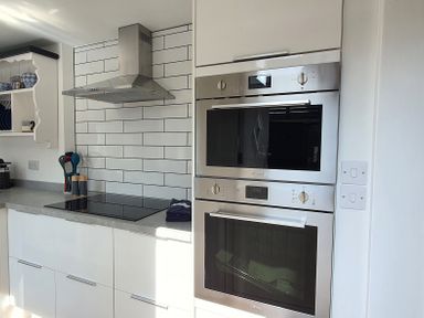 A kitchen with built in ovens a stovetop under a range hood and open shelving with dishes at No.37 in Beverley