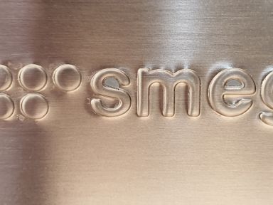 A close up of the embossed smeg logo on a metal surface