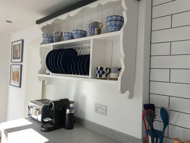 A kitchen counter with a coffee machine, toaster, utensils in a holder and plates, bowls, and mugs on a white wall-mounted shelf at No.37 Beverley