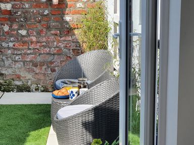 An outdoor patio area with two wicker chairs and a small table with croissants orange juice coffee and a mug at No.37 Beverley