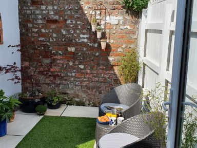 A small outdoor patio with two wicker chairs a table with croissants and drinks plants on the ground and hanging pots on a brick wall at No 37 in Beverley