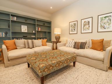 A living room with two sofas a patterned ottoman and a shelving unit at Hawthorn Barn in Northleach