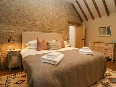 A bedroom with a bed with pillows and folded towels on a blanket a dresser with a mirror and wooden beams on the ceiling at Hawthorn Barn in Northleach