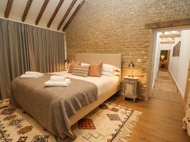 A bedroom with a bed with pillows and folded towels on a rug and wooden beams at Hawthorn Barn in Northleach