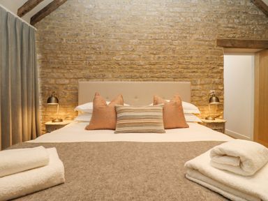 A bedroom with a bed with pillows bedside tables lamps towels on a blanket at Hawthorn Barn in Northleach