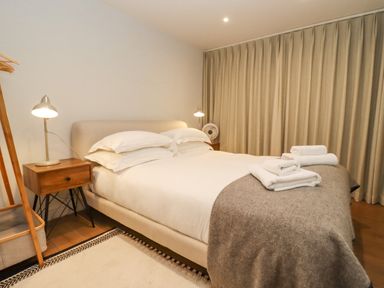 A bedroom with a bed a gray blanket and white towels on top and wooden nightstands at Hawthorn Barn in Northleach