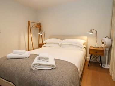 A bedroom with a double bed white pillows and towels bedside tables lamps a clothes rack and a fan at Hawthorn Barn Northleach